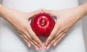 Time for a Healthy Gut Check (woman holding a red apple in front of her stomach)
